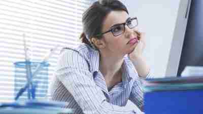 A young woman with ADHD, sitting in front of a computer and thinking "I am so bored at work!"