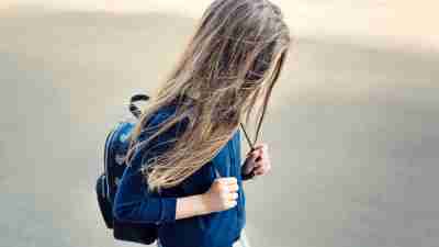 Young girl walking with backpack and long hair covering face